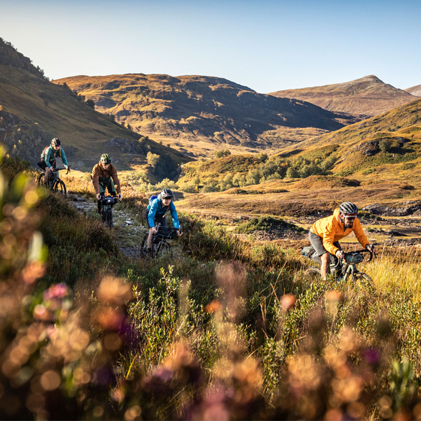 Gruppe von Radfahrern unterwegs in herbstlicher Berglandschaft mit weitem Talblick.